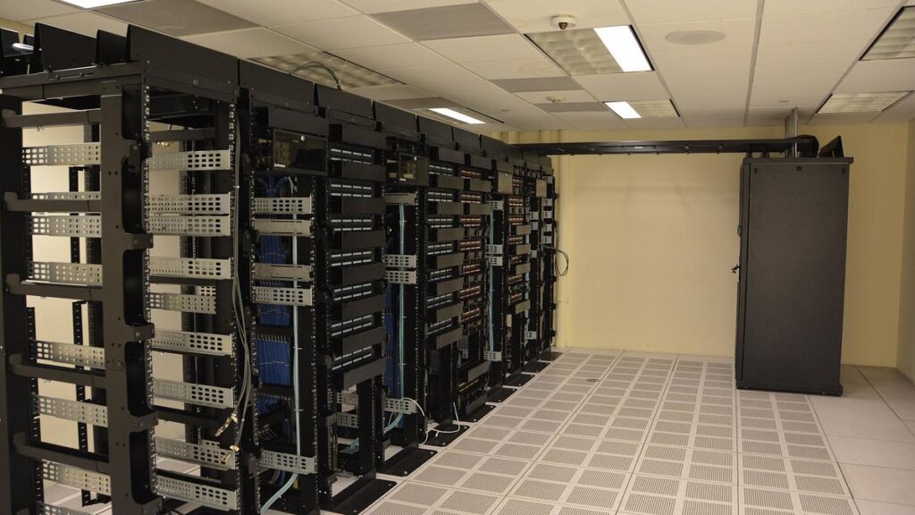 A long aisle of black server racks inside a real data center, the kind of AI compute buildout at the heart of the is-AI-a-bubble debate