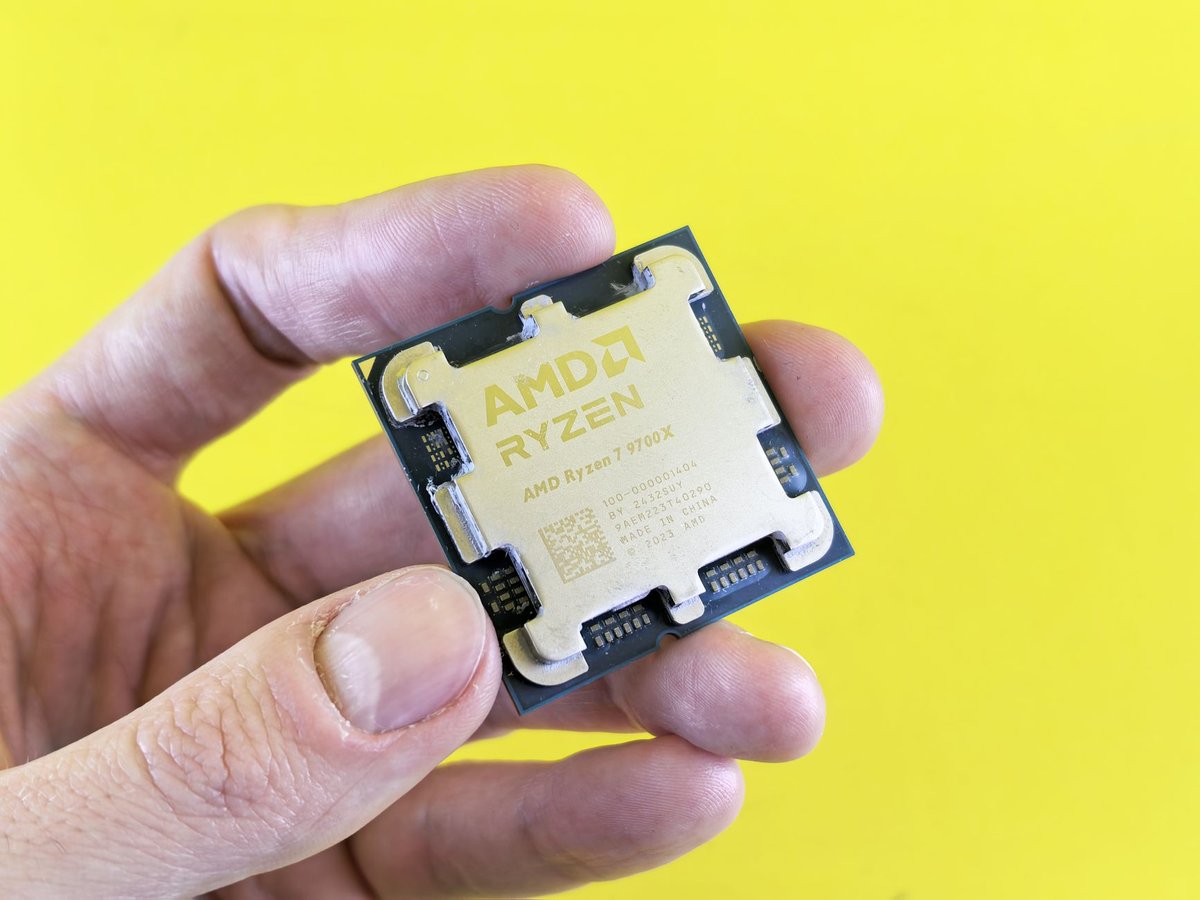 AMD Ryzen 7 9700X processor held between finger and thumb against a yellow background