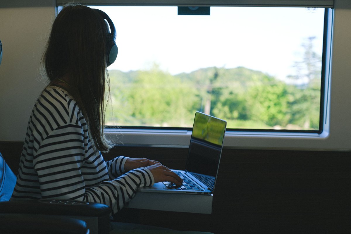Woman working on a laptop beside a train window, unplugged, illustrating all-day battery life on an efficient AI PC