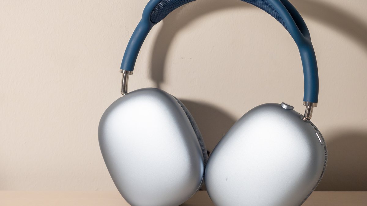 Silver Apple AirPods Max over-ear headphones with a blue headband resting on a desk