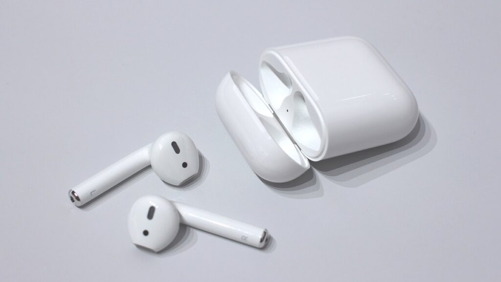 A pair of Apple AirPods with the left and right earbuds beside an open charging case on a light background, illustrating why AirPods may play in only one ear