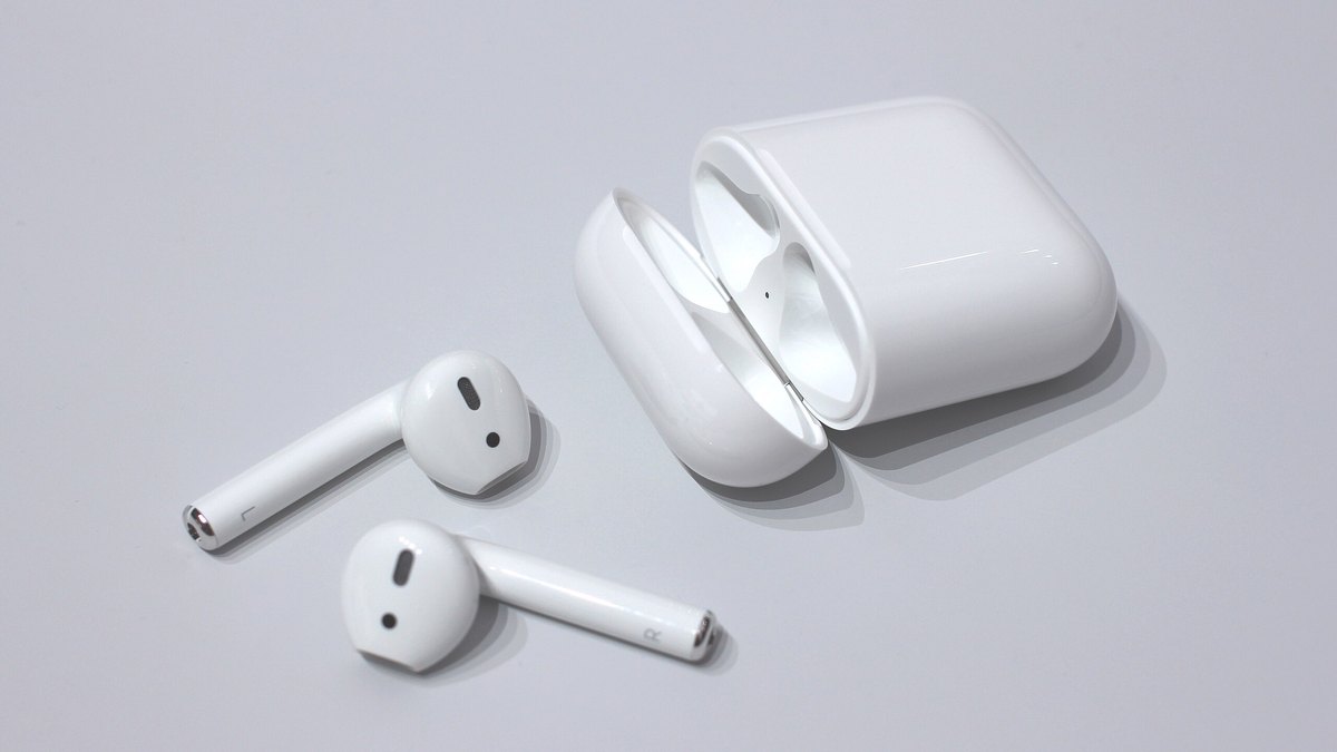 A pair of Apple AirPods with the left and right earbuds beside an open charging case on a light background, illustrating why AirPods may play in only one ear