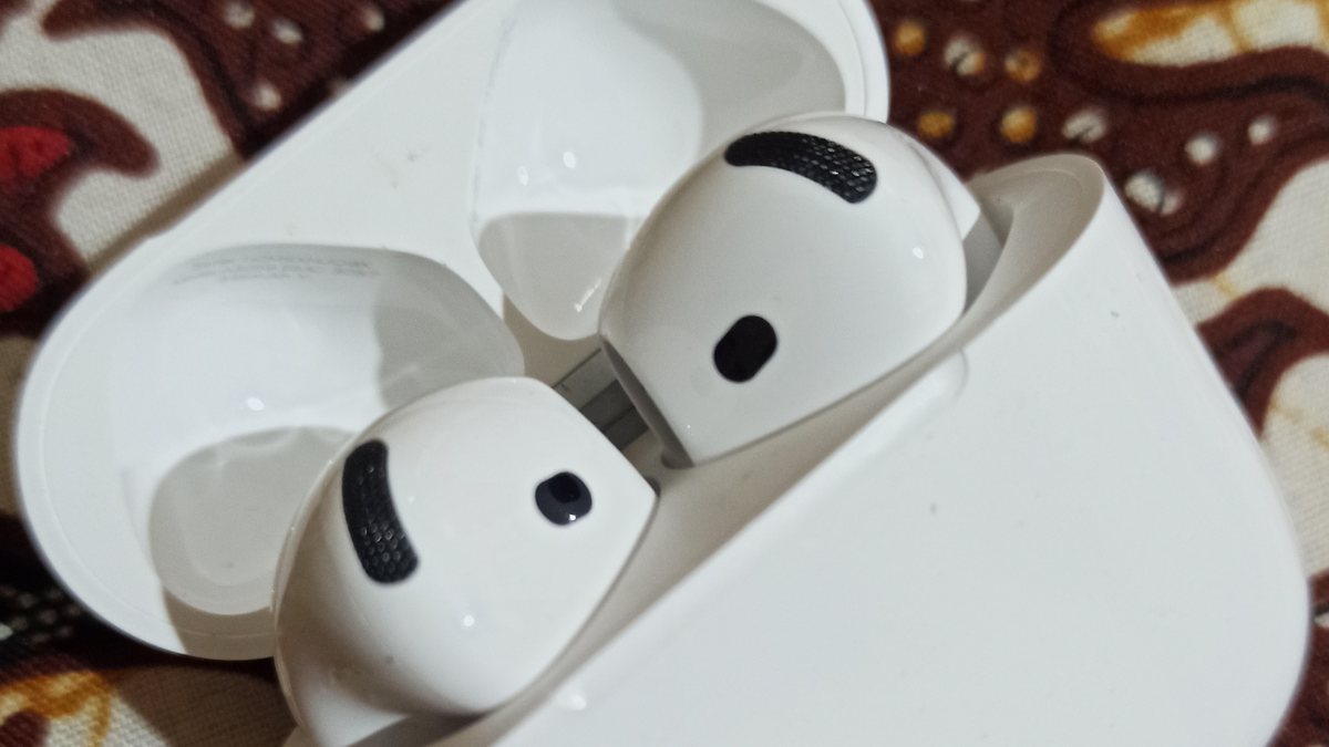 Close-up of two AirPods showing the black oval speaker mesh grille where earwax collects and blocks the sound