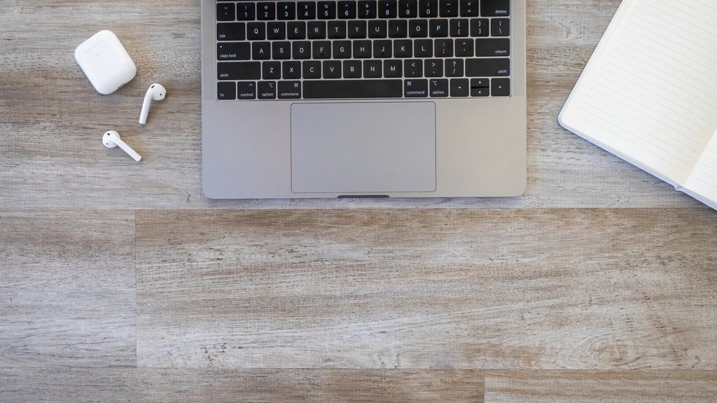 A laptop, wireless earbuds, and a notebook laid out on a wooden desk, the everyday Bluetooth devices whose connections keep dropping