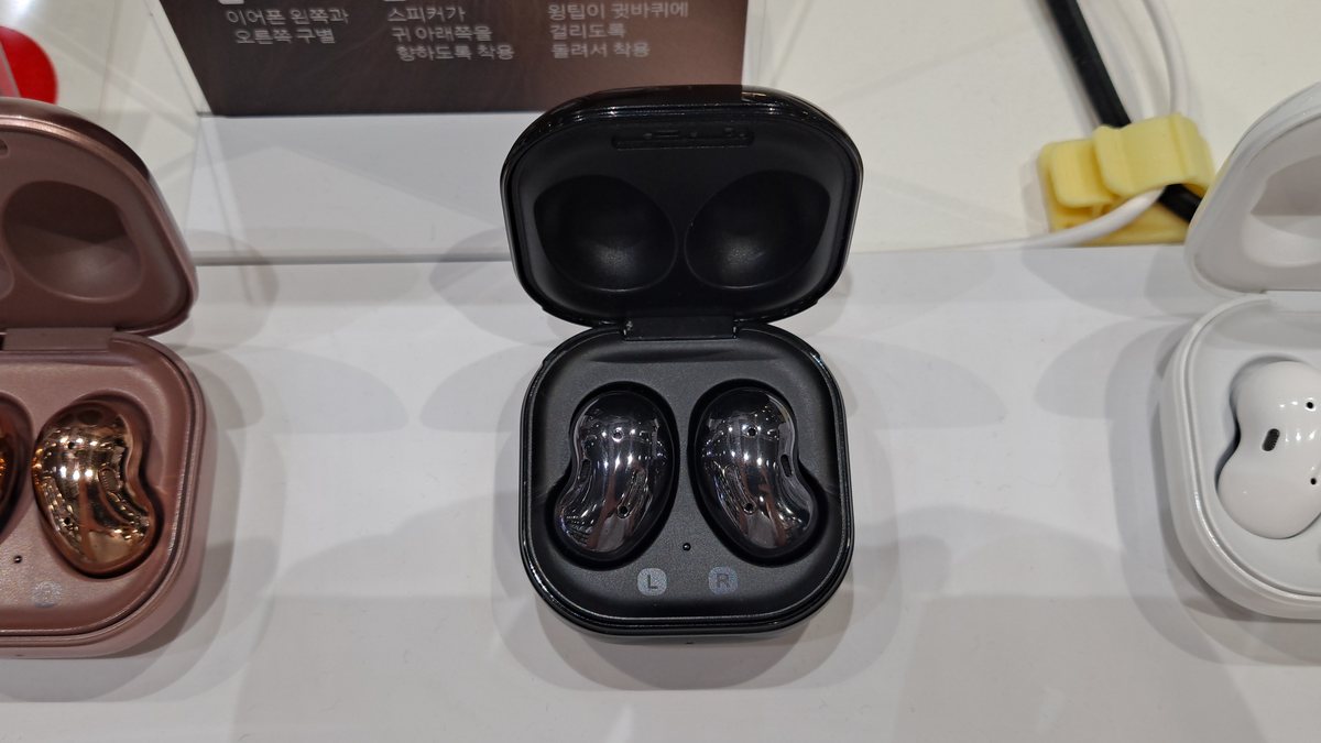 Three sets of Samsung Galaxy Buds Live true-wireless earbuds in bronze, black, and white charging cases on a display shelf