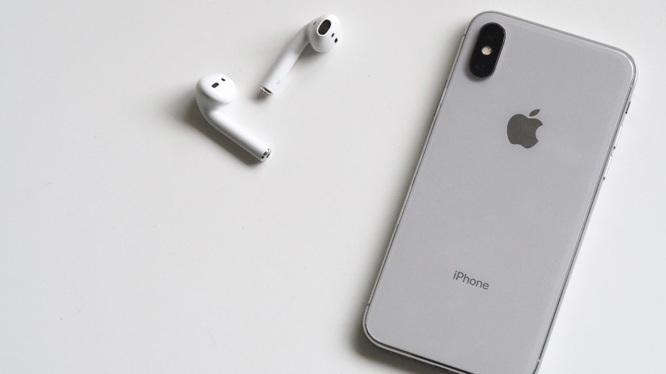 A silver iPhone next to a pair of white AirPods on a plain white surface, the phone-and-earbuds pairing you forget and re-pair to fix drops