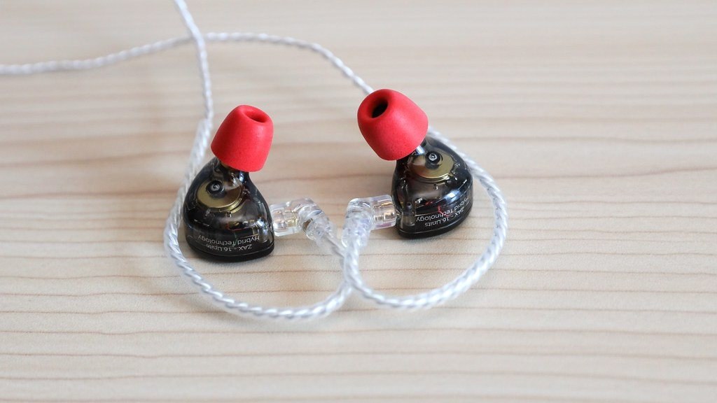A pair of in-ear monitors fitted with red memory foam ear tips resting on a wooden surface