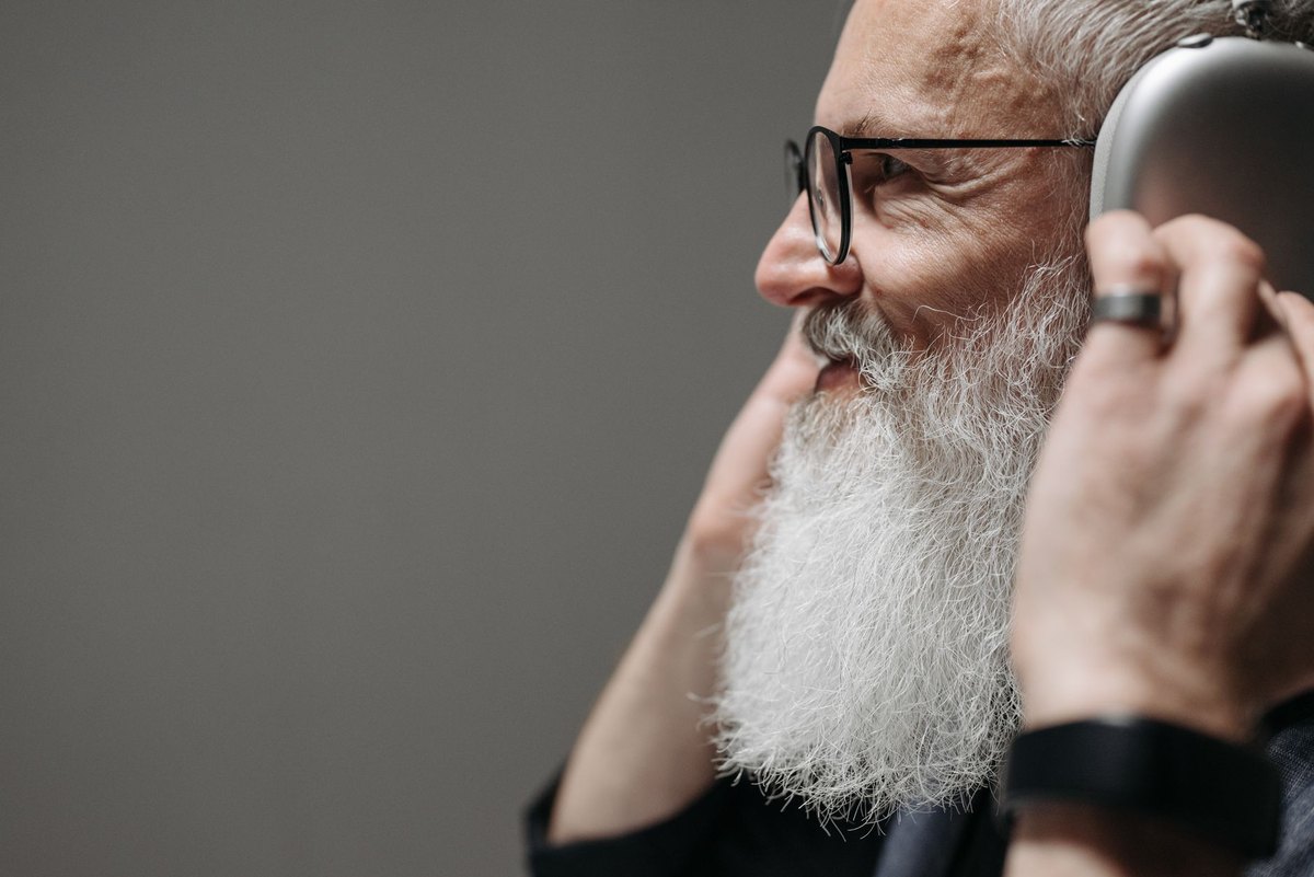 Profile of a man wearing glasses with an over-ear headphone cup at his ear, the temple arm of the frames running back along his head toward the earpad