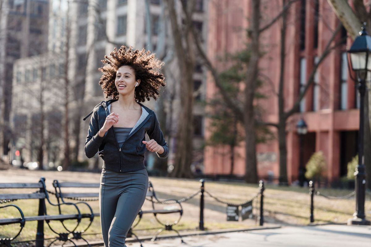 Woman actively running in an urban park wearing a white true wireless earbud with no visible cable
