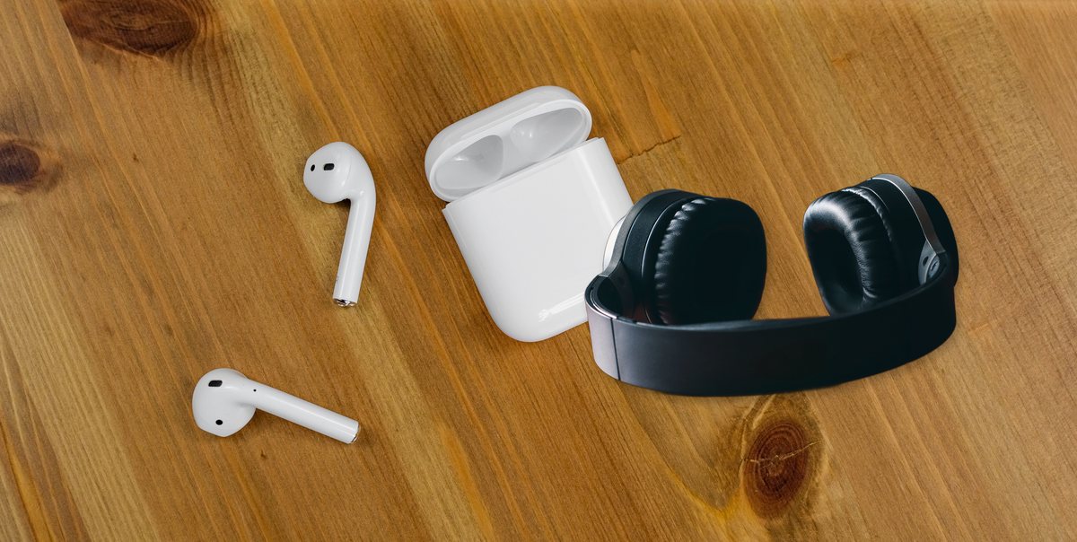 An over-ear headphone pair and a true wireless earbud pair with its open charging case together on a wood desk