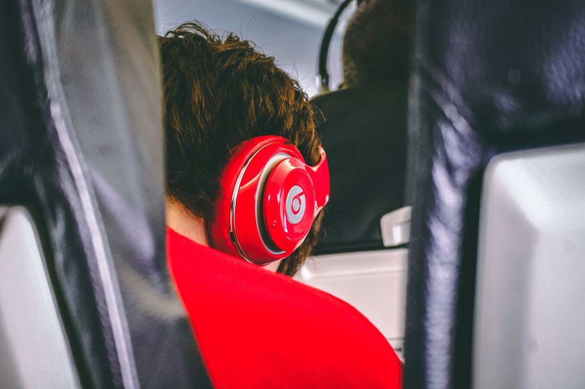 Airline passenger seen from behind wearing red over-ear headphones in a cabin seat