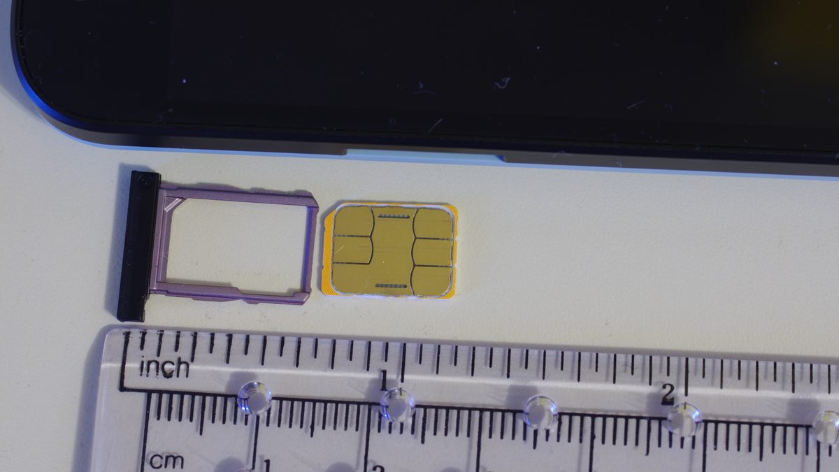 Macro photo of a gold nano-SIM card sitting next to its pink phone SIM tray, with a ruler below showing it is barely an inch wide
