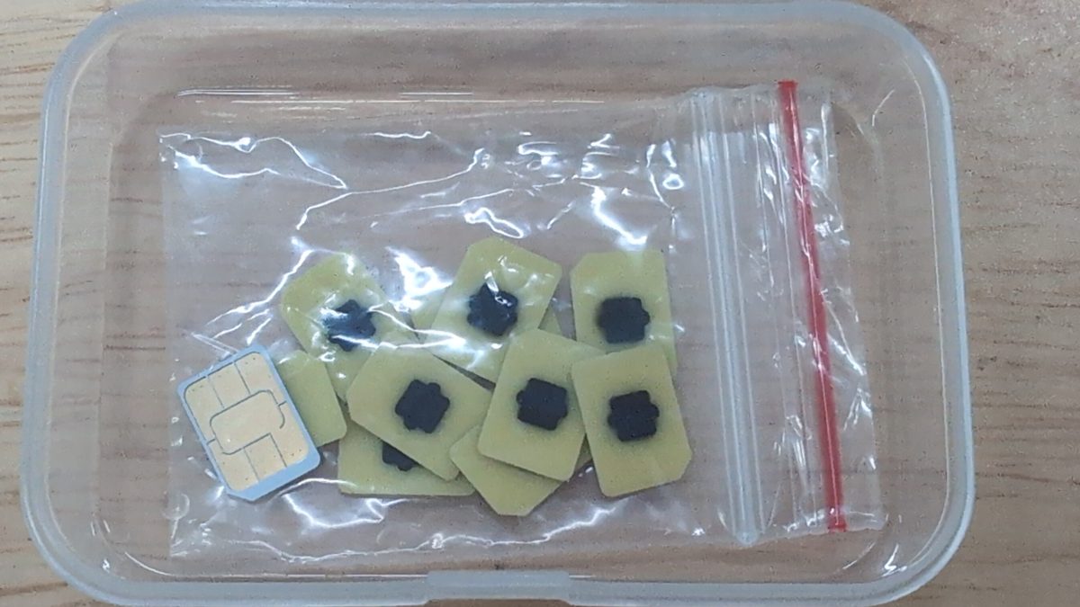 A cluster of tiny eUICC eSIM chips in a plastic bag next to a single nano-SIM cutout, the embedded chips that replace a removable SIM card