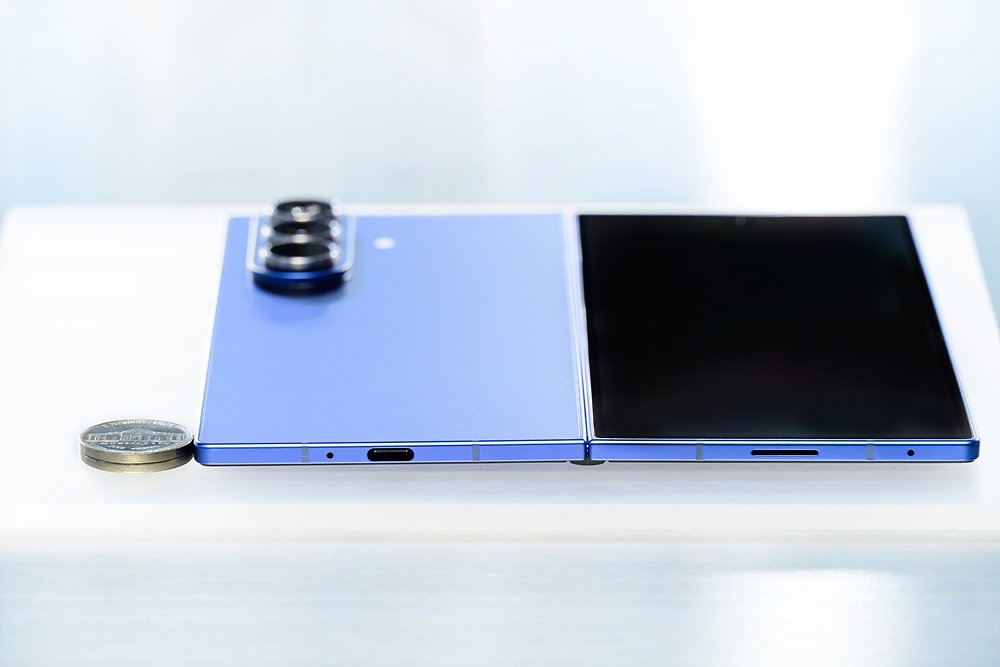 Official Samsung press photo of the Galaxy Z Fold 7 lying unfolded next to a coin to show its 4.2mm thinness
