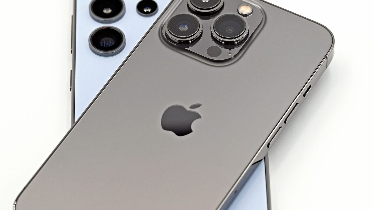 The back of a graphite iPhone 13 Pro resting on top of a light-blue Samsung Galaxy S24 Ultra, both camera systems visible, showing how iPhone and Android hardware differ