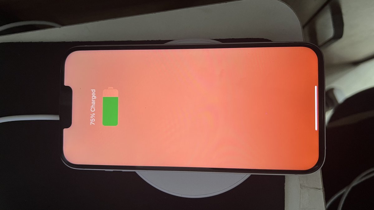 A real iPhone resting on a wireless charging pad with the screen showing 75% Charged and a green battery icon