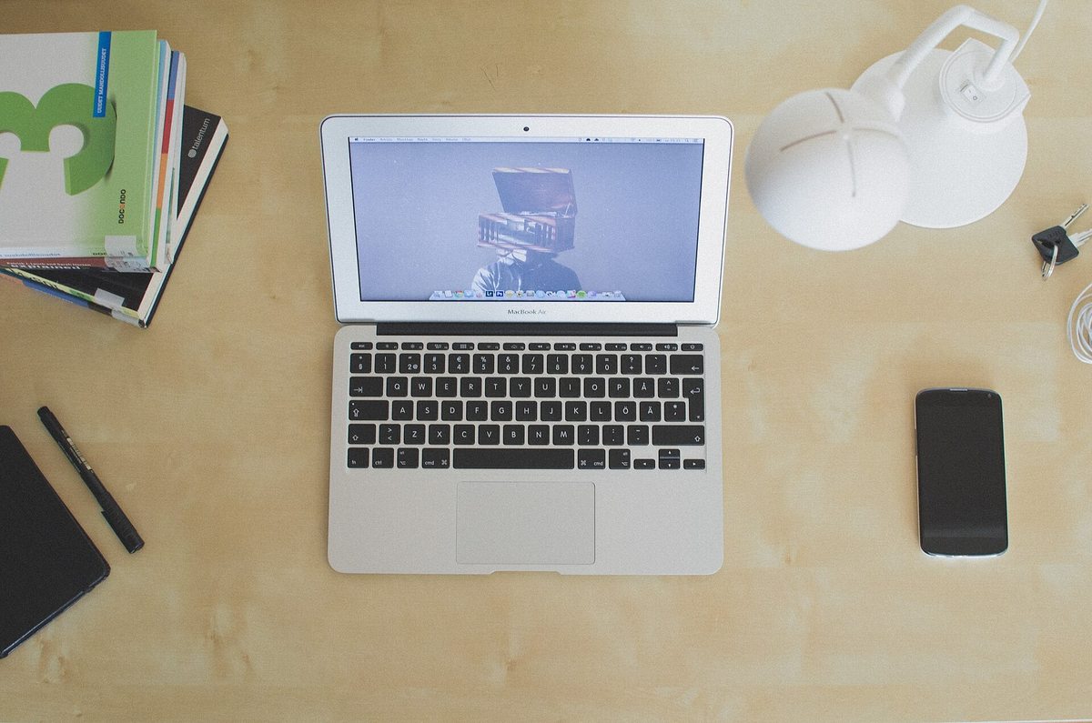 An open MacBook Air laptop sitting on a desk beside headphones and a phone
