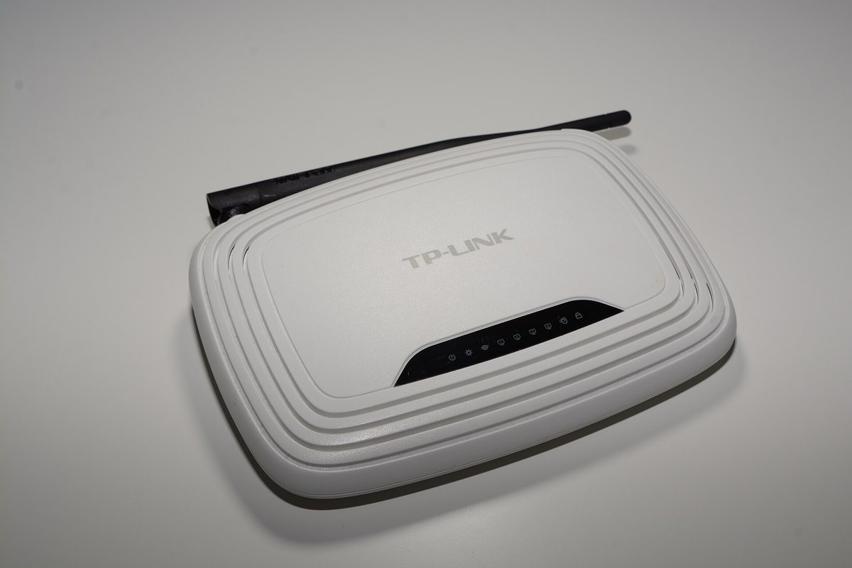 A white TP-Link home Wi-Fi router with a single antenna and status LEDs, the device whose DHCP hands network printers a new IP after a reboot