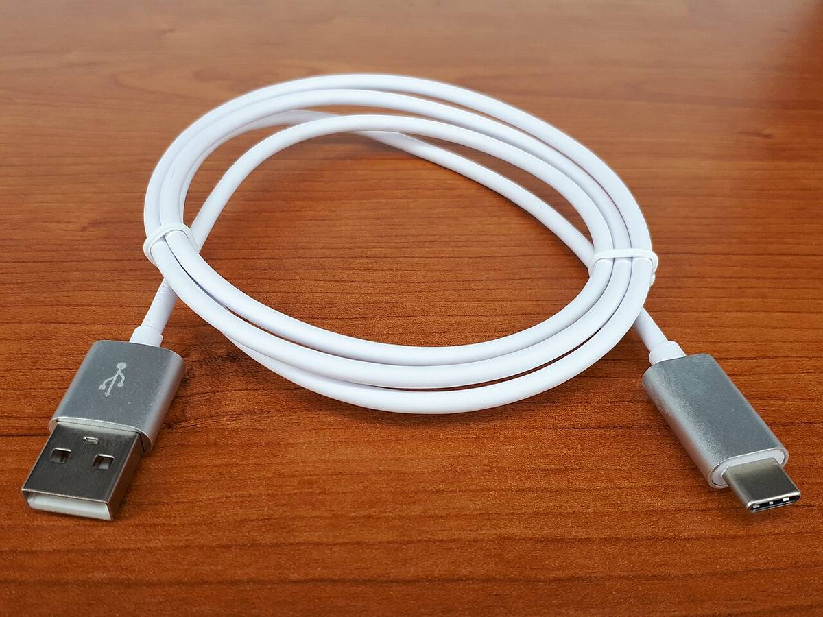 A white USB-C to USB-A cable coiled on a wooden desk, the kind of cable that may be charge-only and unable to pass a pairing signal