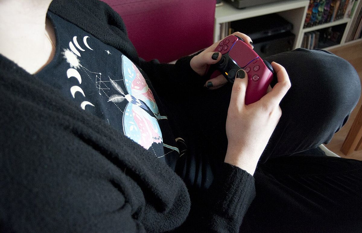 Hands holding a Cosmic Red DualSense controller mid-game, the same controller that pairs to a PC over USB or Bluetooth