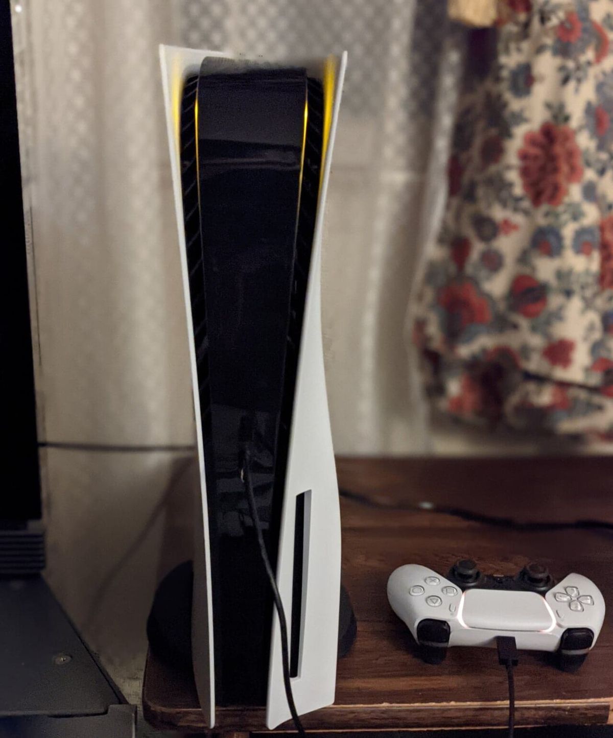 A white PS5 console standing next to a white DualSense controller with a cable, the wired USB-C setup that forces a controller to re-pair