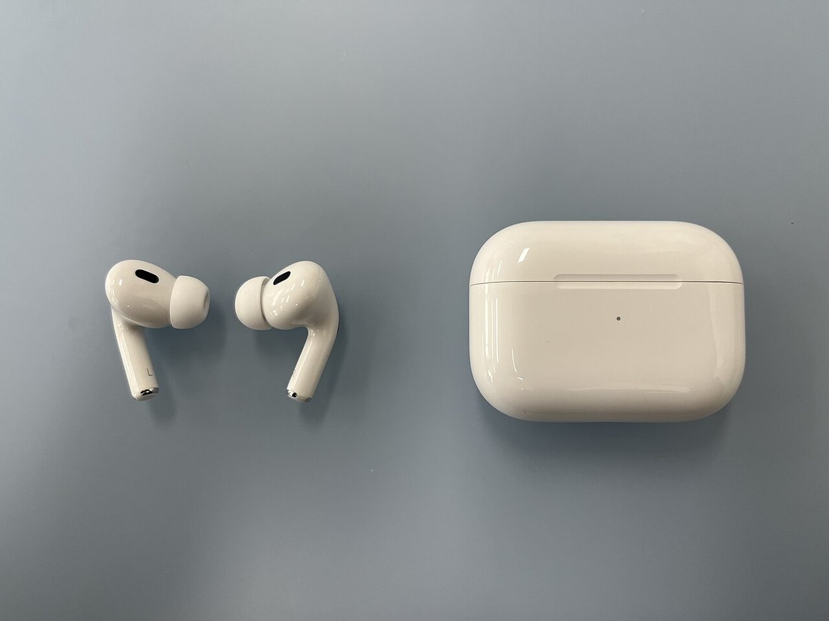 Apple AirPods Pro (2nd generation) earbuds lying next to their closed white MagSafe charging case on a blue-grey surface