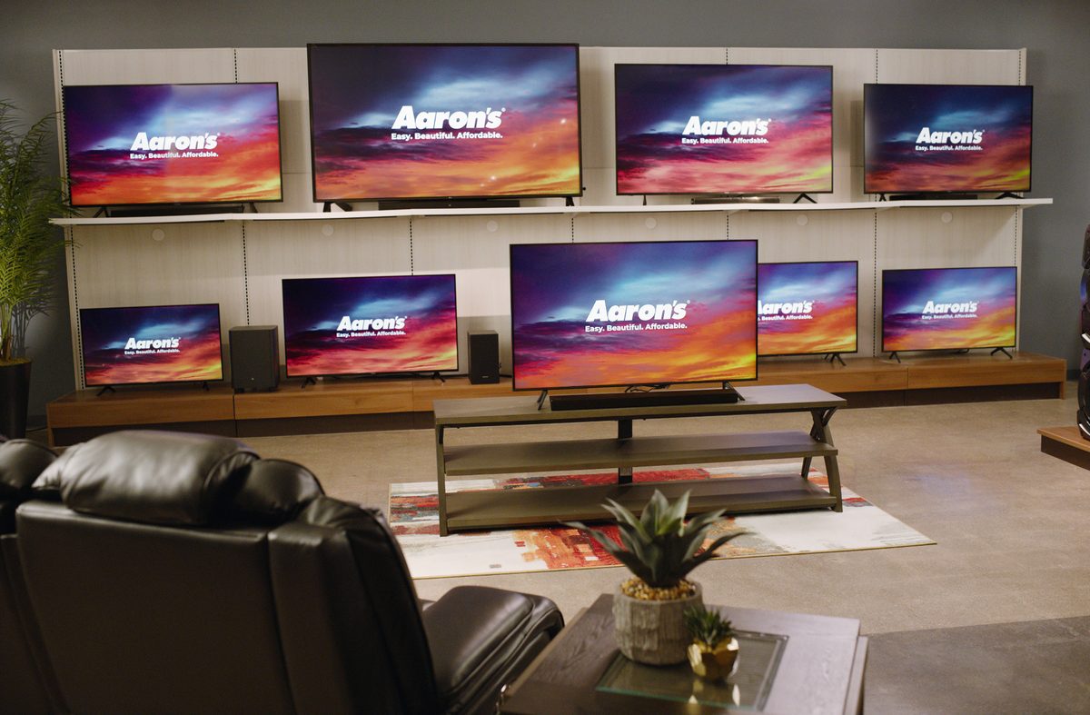 A retail showroom wall lined with many flat-screen televisions all displaying a colorful sunset, representing the choice a TV shopper faces
