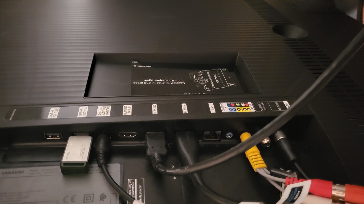 The rear input panel of a Samsung TV showing labeled HDMI IN 1, 2 and 3 (ARC) ports, USB, LAN and power connections with cables plugged in