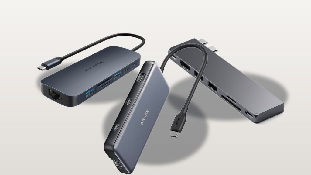 Three real USB-C hubs for MacBook, a HyperDrive Next, an Anker 555, and a Satechi Pro Hub Slim, arranged on a neutral studio background